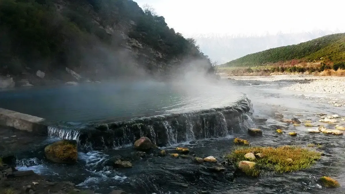 Ujëra termale me avull që ngrihet në një peizazh natyror malor në Shqipëri, duke sugjeruar veti shëruese.
