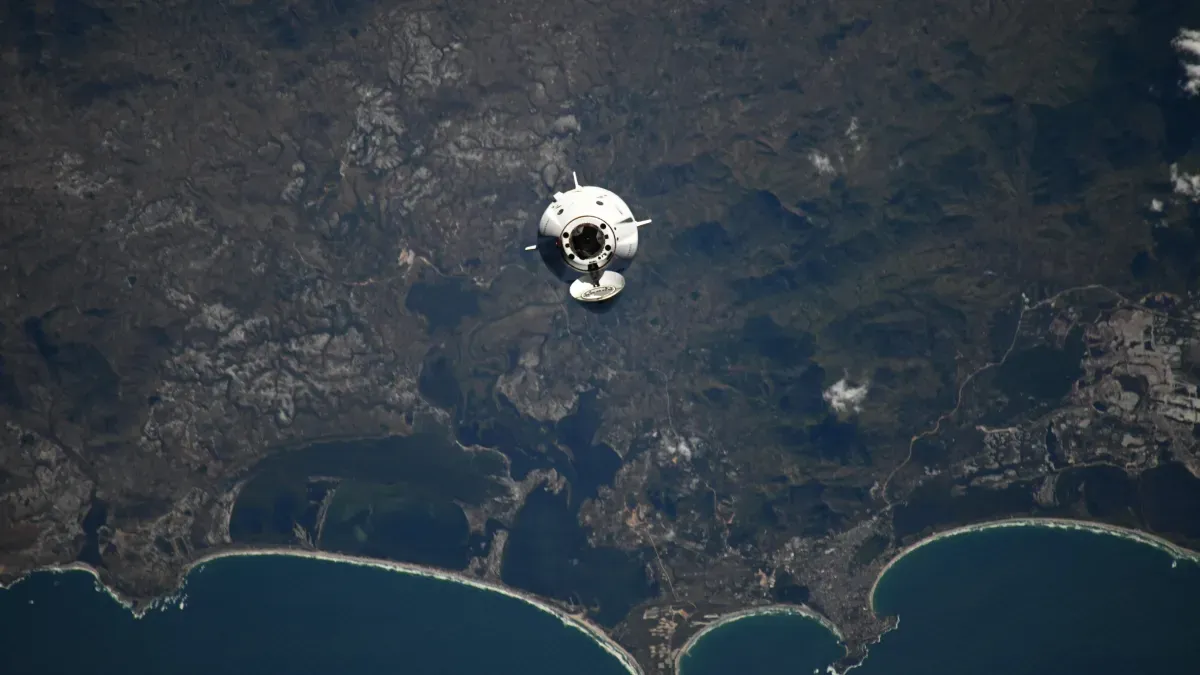 Një anije kozmike ose satelit duke rrotulluar rreth Tokës, me një pamje të detajuar të kontinentit dhe detit poshtë.