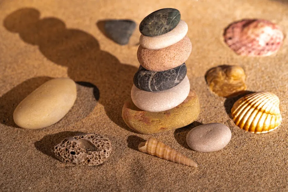 Gurë të ekuilibruara dhe guaska me shpiron në rërë krijojnë një skenë të qetë