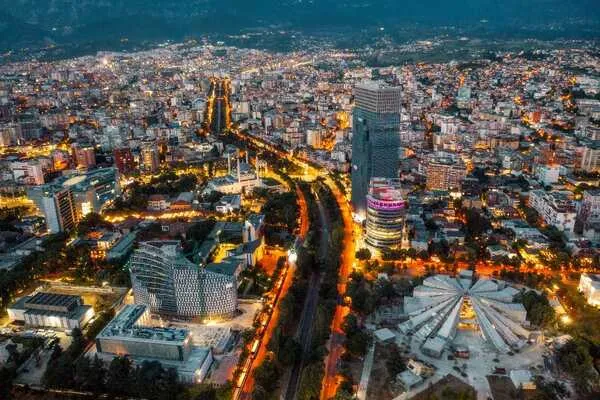 Pamje ajrore e Tiranës, Shqipëri në muzg, me drita qyteti të ndezura, duke treguar urbanizmin dhe potencialin e qyteteve inteligjente.
