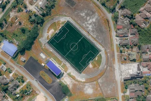 Pamje nga lart e një fushe futbolli lokale me pistë atletike, simbol i projektit "100 Fushat".