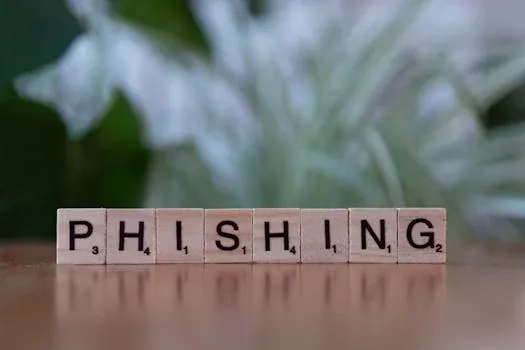 Pllaka scrabble që formojnë fjalën "PHISHING" mbi një sipërfaqe druri, duke ilustruar rrezikun e mashtrimit online dhe strategjitë e mbrojtjes.